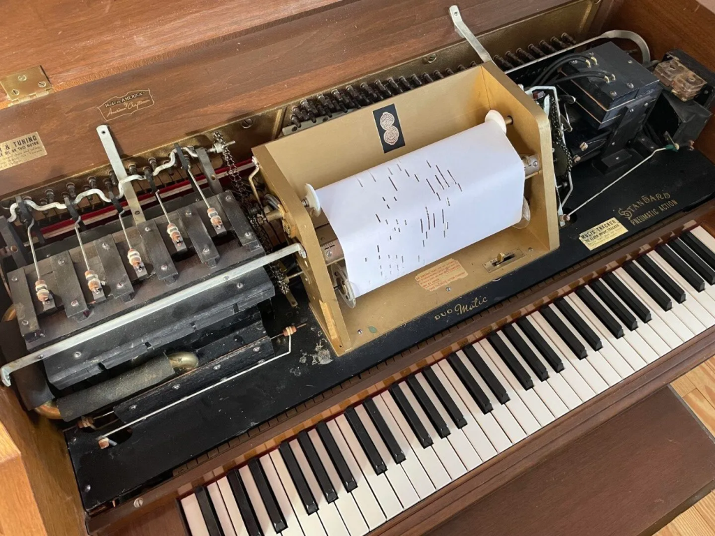 Player piano with exposed mechanism and roll.