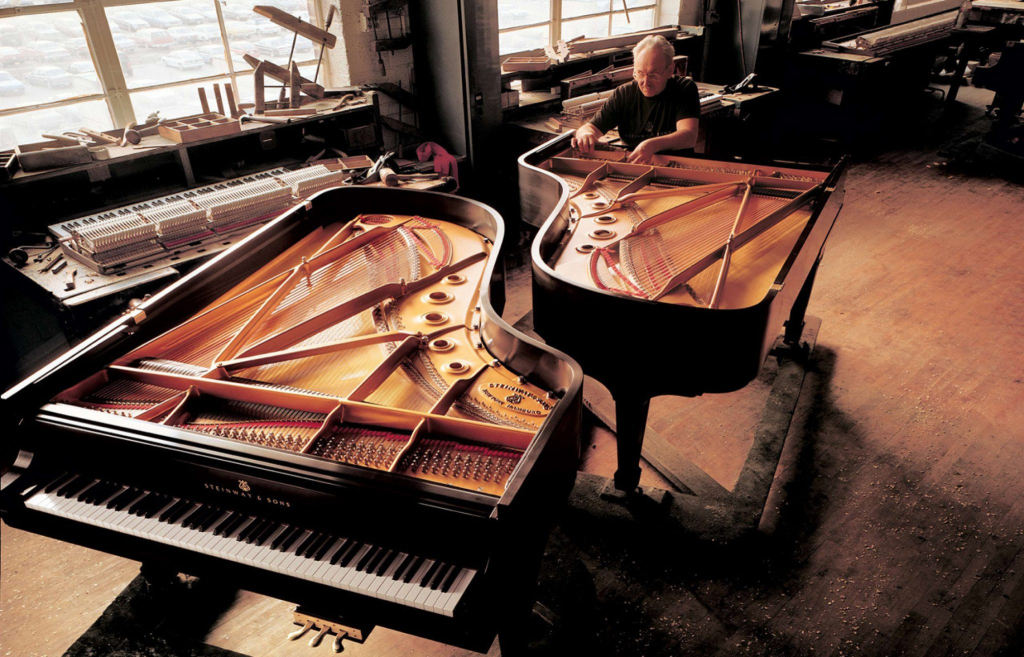Man tuning grand pianos in workshop.