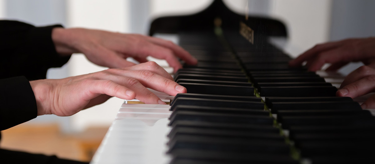 Hands playing a piano keyboard.