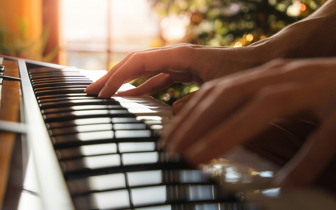 Hands playing piano with sunlight background.