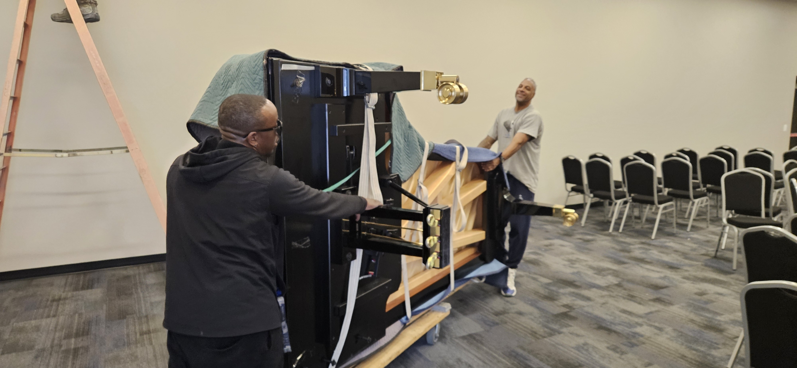 Two people moving a grand piano indoors.
